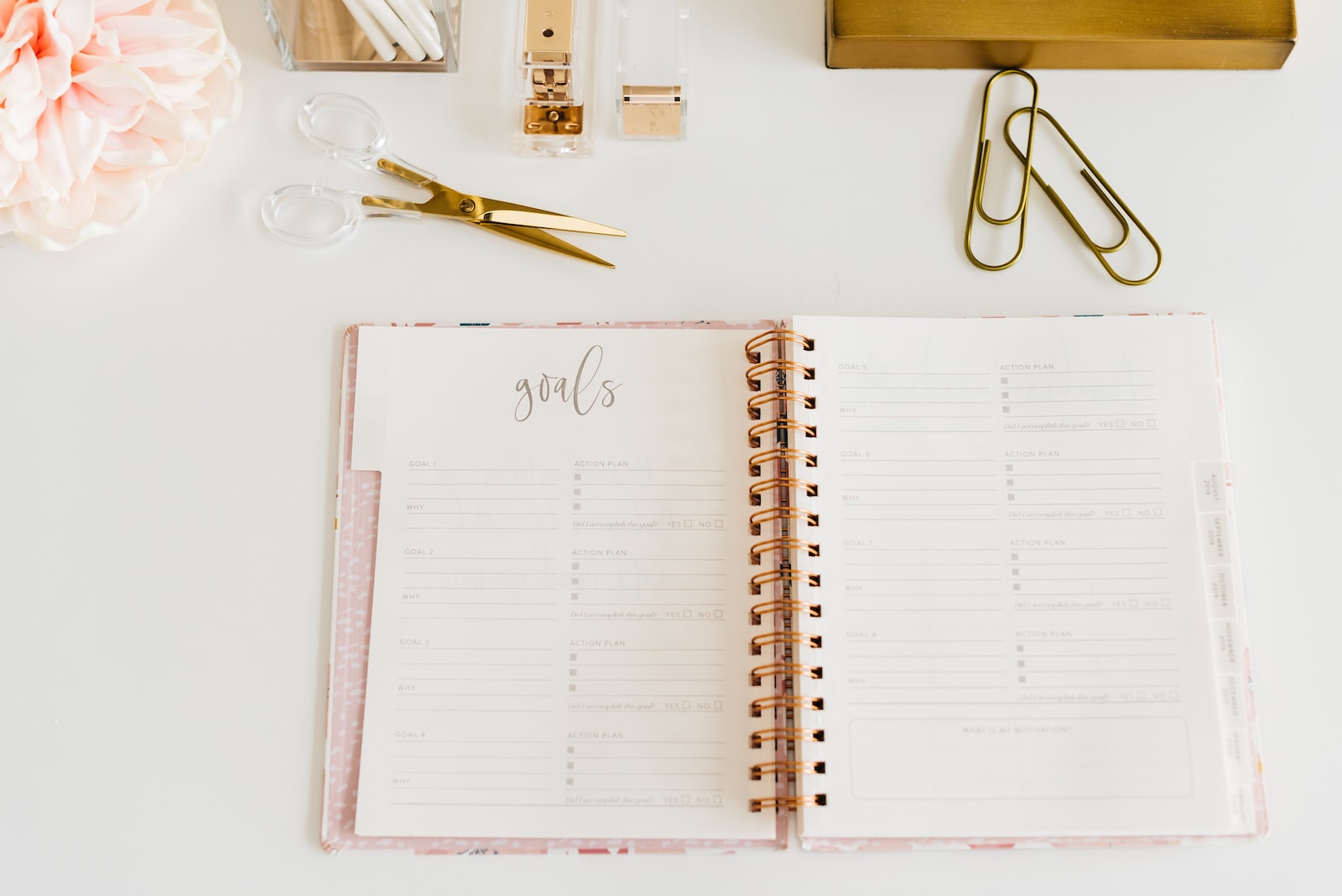 scissors and two paper clips beside opened spiral notebook business goals